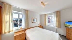 A hotel room with a bed, a nightstand, a lamp, a window with curtains, and a television.