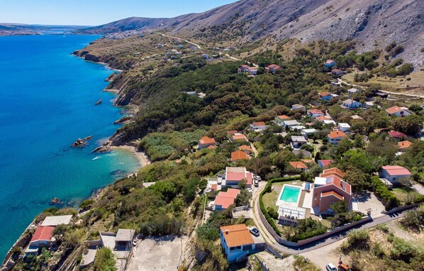 Un village côtier avec des maisons, une mer d’un bleu limpide et un paysage montagneux en arrière-plan.