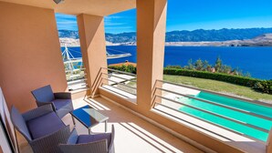 A balcony with a view of a lake and mountains, wicker furniture, and a pool. - 5 bedroom awesome home in Pag (Pag)