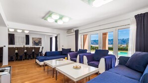 A modern living room with a dining area, large windows with a mountain view, and a pool visible through the glass doors. - 5 bedroom awesome home in Pag (Pag)