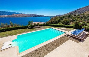Une piscine rectangulaire à l’eau d’un bleu limpide, entourée d’une terrasse dallée et d’un petit jardin agrémenté d’une pergola.