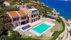 A two-story house with a swimming pool, a patio with lounge chairs, and a view of the sea. - 5 bedroom awesome home in Pag (Pag)