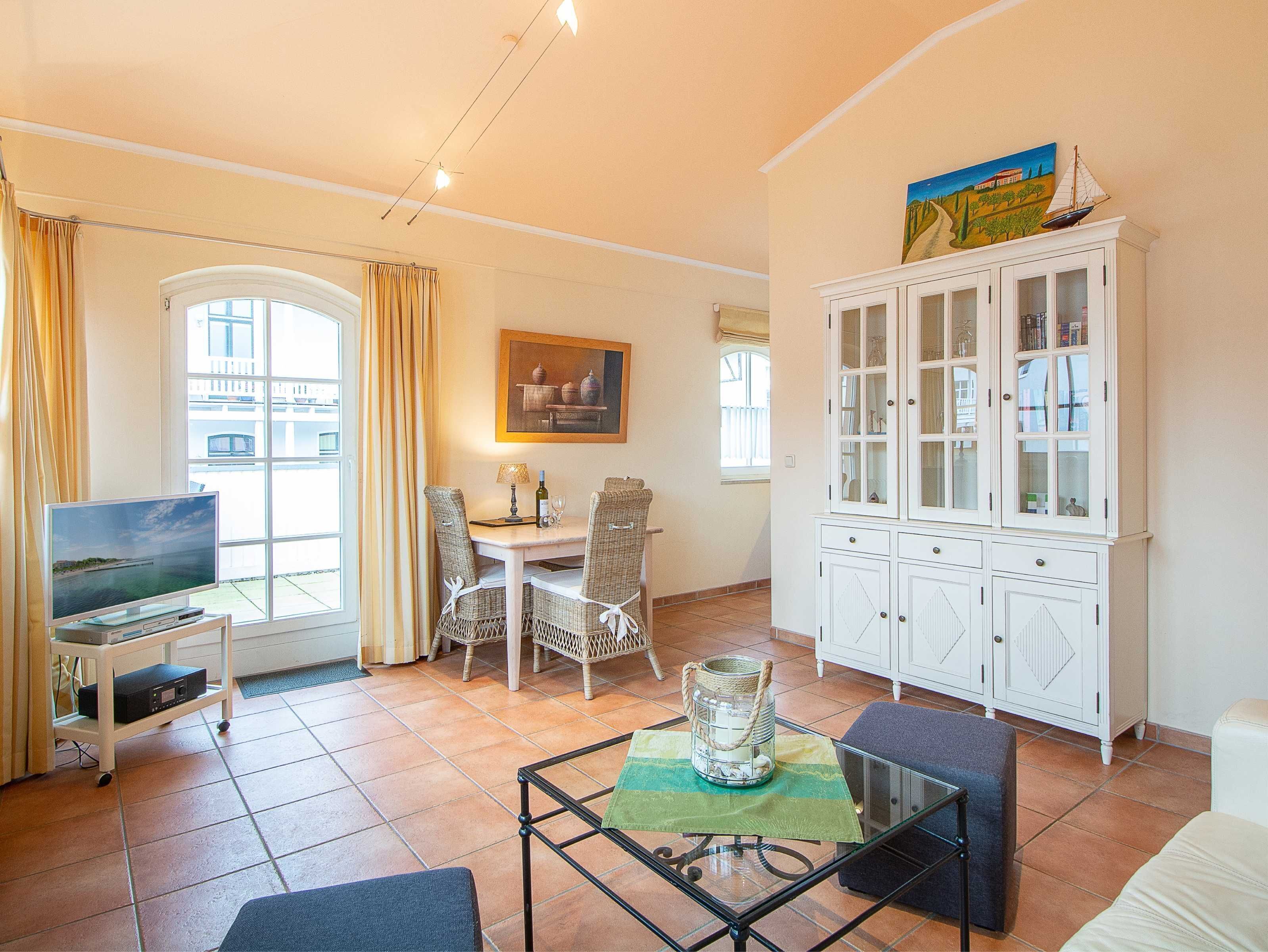 A living room with a TV, dining table, chairs, a glass-top coffee table, and a white cabinet.