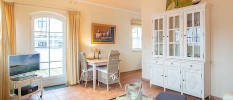 A living room with a TV, dining table, chairs, a glass-top coffee table, and a white cabinet.