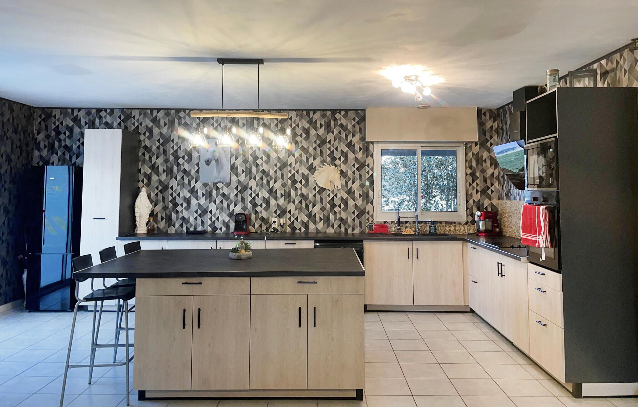 A modern kitchen with a central island, light wood cabinets, a patterned backsplash, and a window providing natural light.