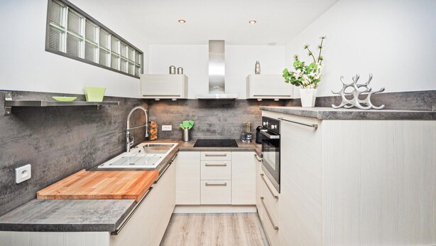 Een moderne keuken met een houten aanrechtblad, roestvrijstalen apparatuur en een grijze spatwand.