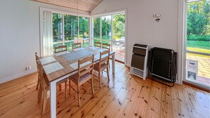 Un comedor con una mesa y sillas de madera, una chimenea y ventanas amplias con vista a un jardín.