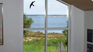 Una habitación con un ventanal grande que da a una masa de agua, un modelo de velero y un pájaro volando afuera.