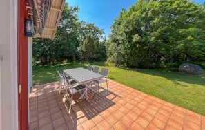 Eine Terrasse mit Tisch und Stühlen, umgeben von einem Garten und Bäumen.