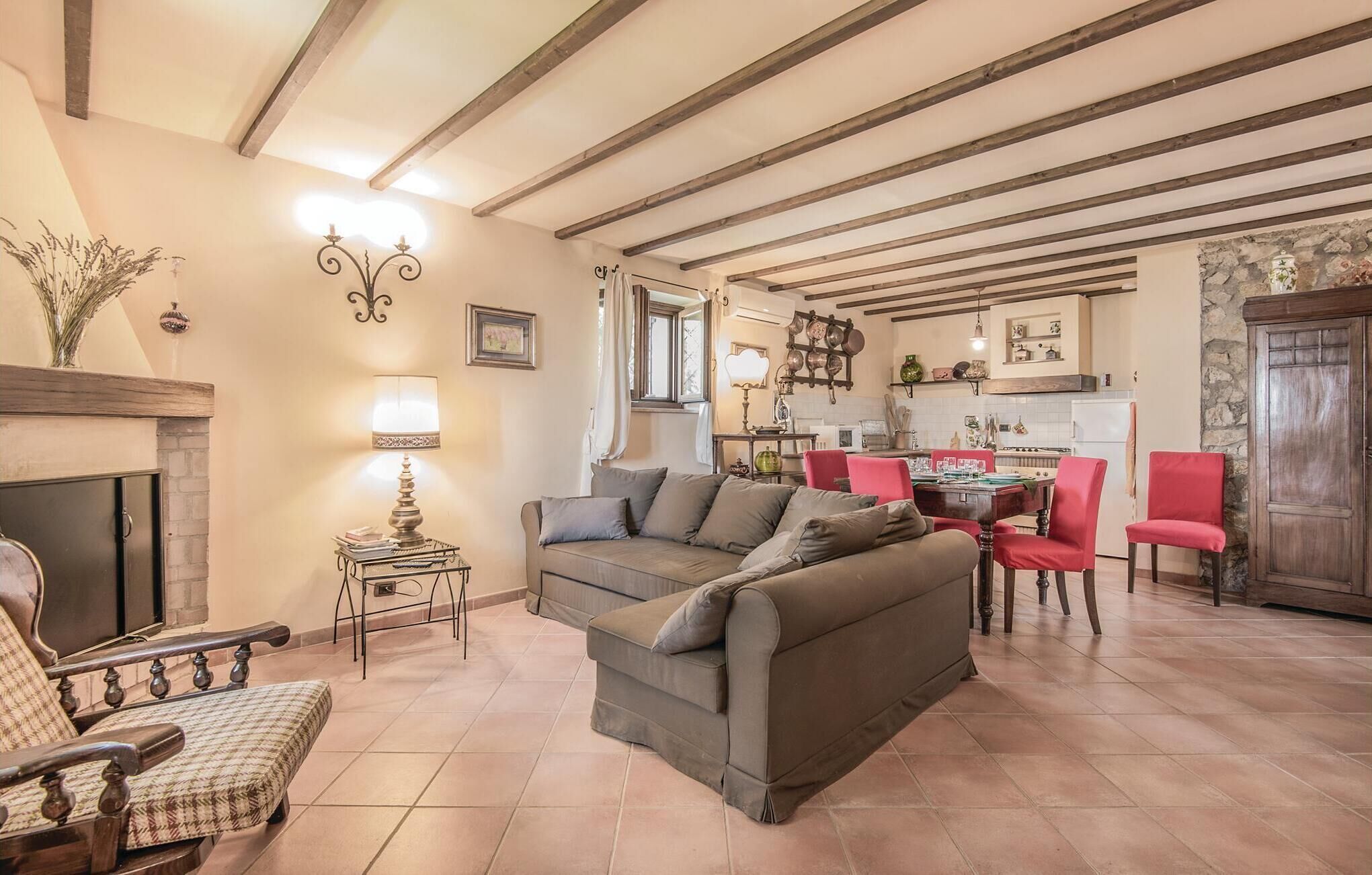 A cozy living room with a sofa, armchairs, and a dining table set for four. A fireplace is visible on the left, and the room has exposed wooden beams on the ceiling.