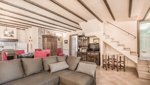A living room with a sectional sofa, a dining area with red chairs, a kitchen with a stove and refrigerator, and a staircase leading to a bathroom.