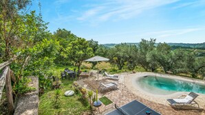 A backyard with a swimming pool, outdoor furniture, and a view of the countryside.