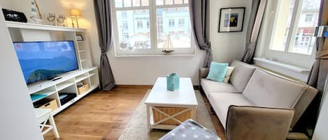 A living room with a television, sofa, coffee table, and a view of buildings outside.