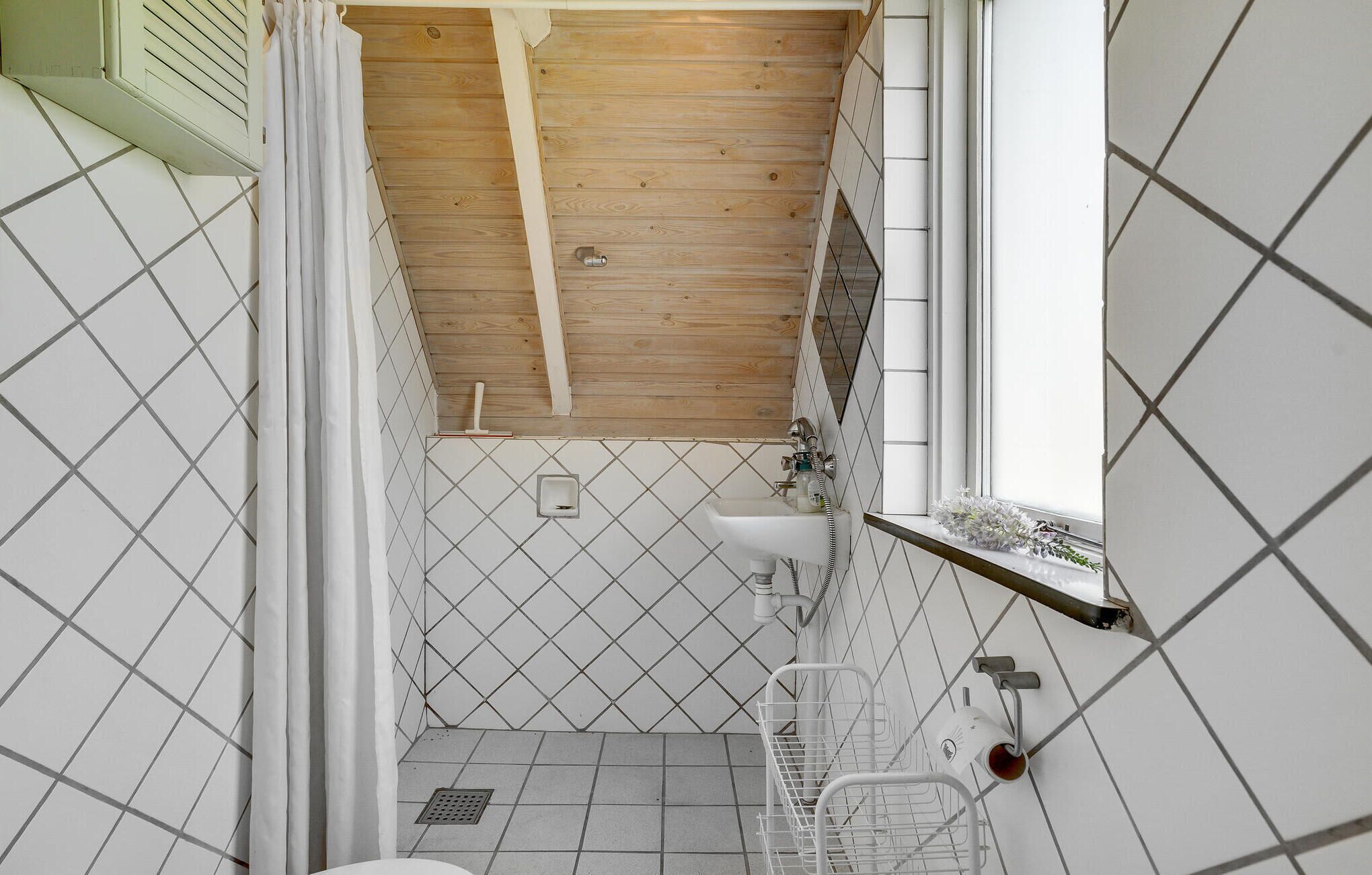 A small, narrow bathroom with a wooden ceiling, a white sink, and a window.