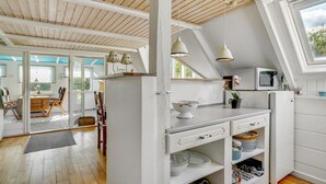 Une cuisine avec des meubles blancs, un plafond en bois et une vue sur l’extérieur.