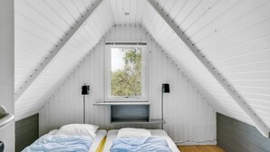 Une petite chambre à coucher de style mansardé, avec deux lits, une fenêtre et un banc intégré.
