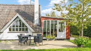 Une maison avec un toit en tuiles, un petit jardin avec une table et des chaises, et un abri de jardin rouge.