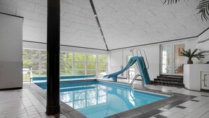 An indoor swimming pool with a blue slide, large windows, and a tiled floor. - Nice home in Ebeltoft with kitchen (Ebeltoft)