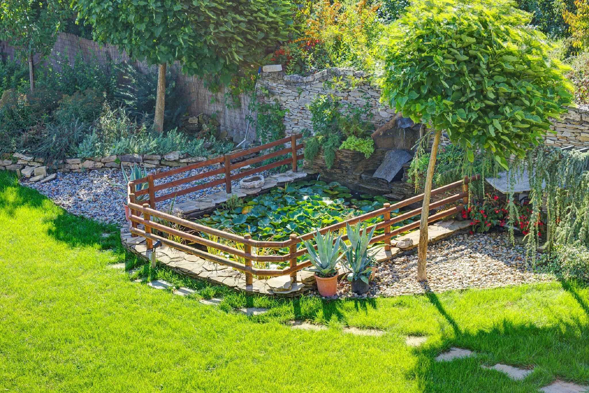 Un jardin avec un pont en bois, un étang et diverses plantes.