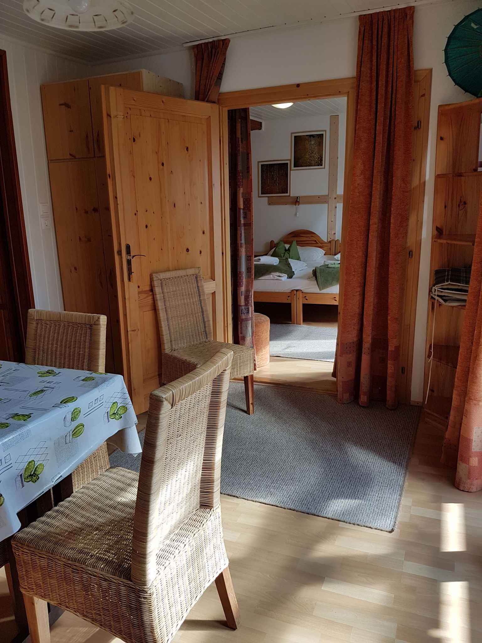 A cozy room with a dining table, wicker chairs, a bed with a wooden headboard, and a wardrobe.