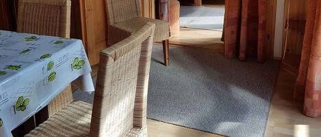 A cozy room with a dining table, wicker chairs, a bed with a wooden headboard, and a wardrobe.