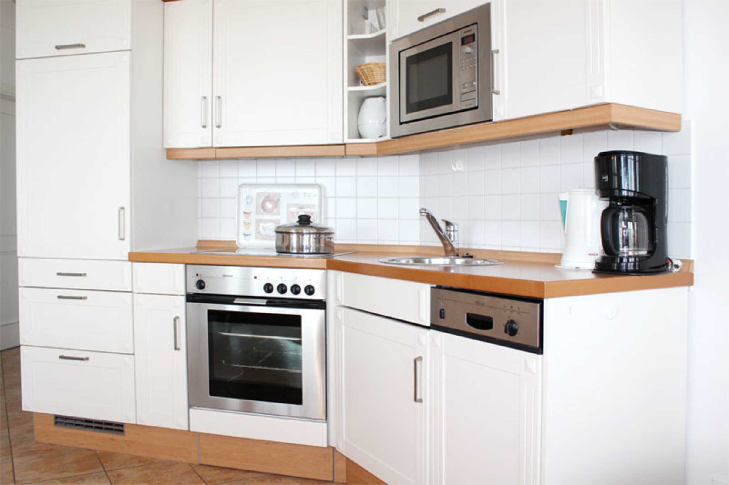 Una cocina moderna con armarios blancos, horno de acero inoxidable, microondas y cafetera.