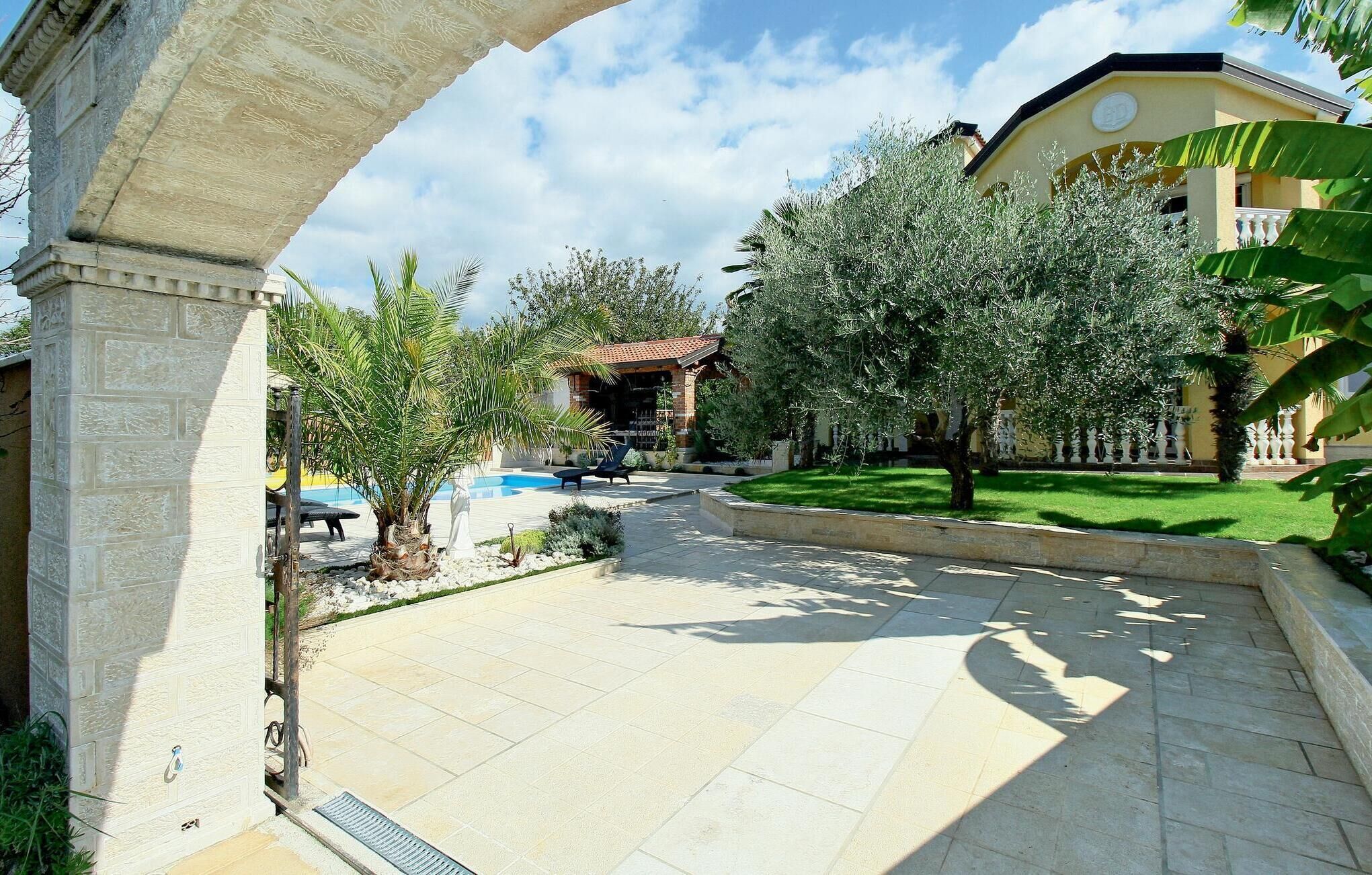 A courtyard with a swimming pool, palm trees, and a building with a yellow facade.