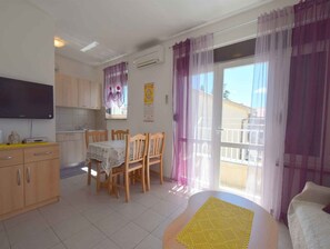 Un espace de vie compact comprenant un coin repas, une kitchenette et un balcon agrémenté de rideaux.