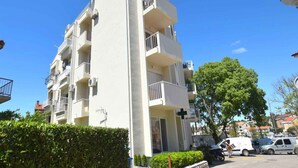Un edificio residencial de varios pisos con balcones, una cruz en la fachada y vehículos estacionados al frente.