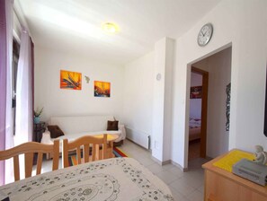 Une pièce comprenant un lit, un canapé, une table à manger avec des chaises, une horloge au mur et deux tableaux.
