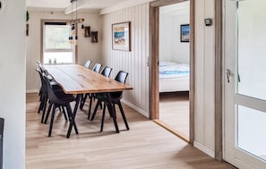 A dining area with a wooden table and black chairs, a window with plants, and a bed in the adjacent room. - Gorgeous home in Thisted with sauna (Thisted)