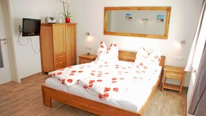 Un dormitorio con una cama de madera, un televisor montado en la pared, una mesita de noche pequeña y un espejo sobre la cama.
