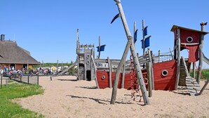 Una playa con un área de juegos de piratas de madera, que incluye un bote salvavidas y una torre de vigilancia.