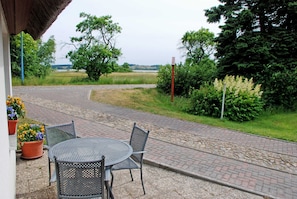 Une terrasse avec une table ronde en métal et deux chaises, entourée de plantes en pot fleuries.