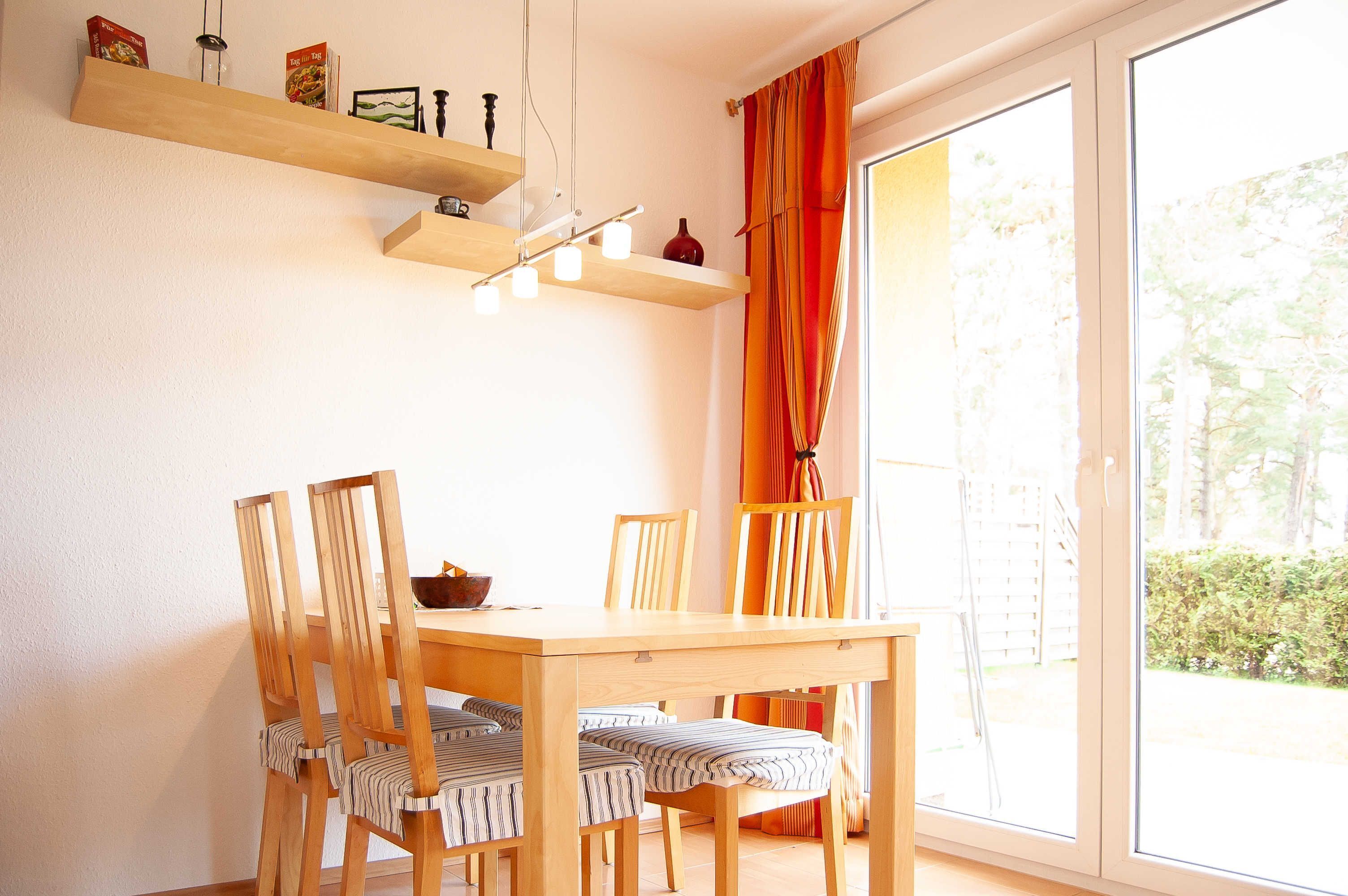 Ein Essbereich mit Holztisch und -stühlen, einer Hängelampe und Blick durch ein großes Fenster.