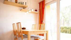 Un coin repas avec une table et des chaises en bois, un luminaire suspendu et une vue dégagée sur l’extérieur grâce à une grande fenêtre.
