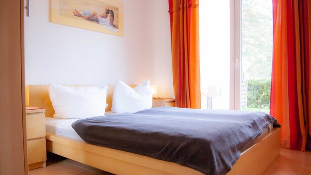 Une chambre à coucher avec un lit, une table de chevet, une commode, une fenêtre avec des rideaux et un tableau au mur.