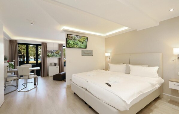 A hotel room with a large bed, a desk with a chair, a TV on the wall, and a view of the outdoors.
