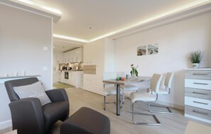 A modern living room with a sofa, a dining table with chairs, a kitchen in the background, and a small plant on a cabinet.