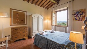 Une chambre à coucher comprenant un lit, une armoire, une commode, une lampe, un tableau et une fenêtre donnant sur un paysage.
