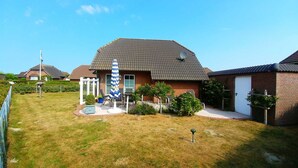 Ein Wohnhaus mit Ziegeldach, einer Satellitenschüssel und einem kleinen Garten mit Rasen und einem blau-weiß gestreiften Sonnenschirm.