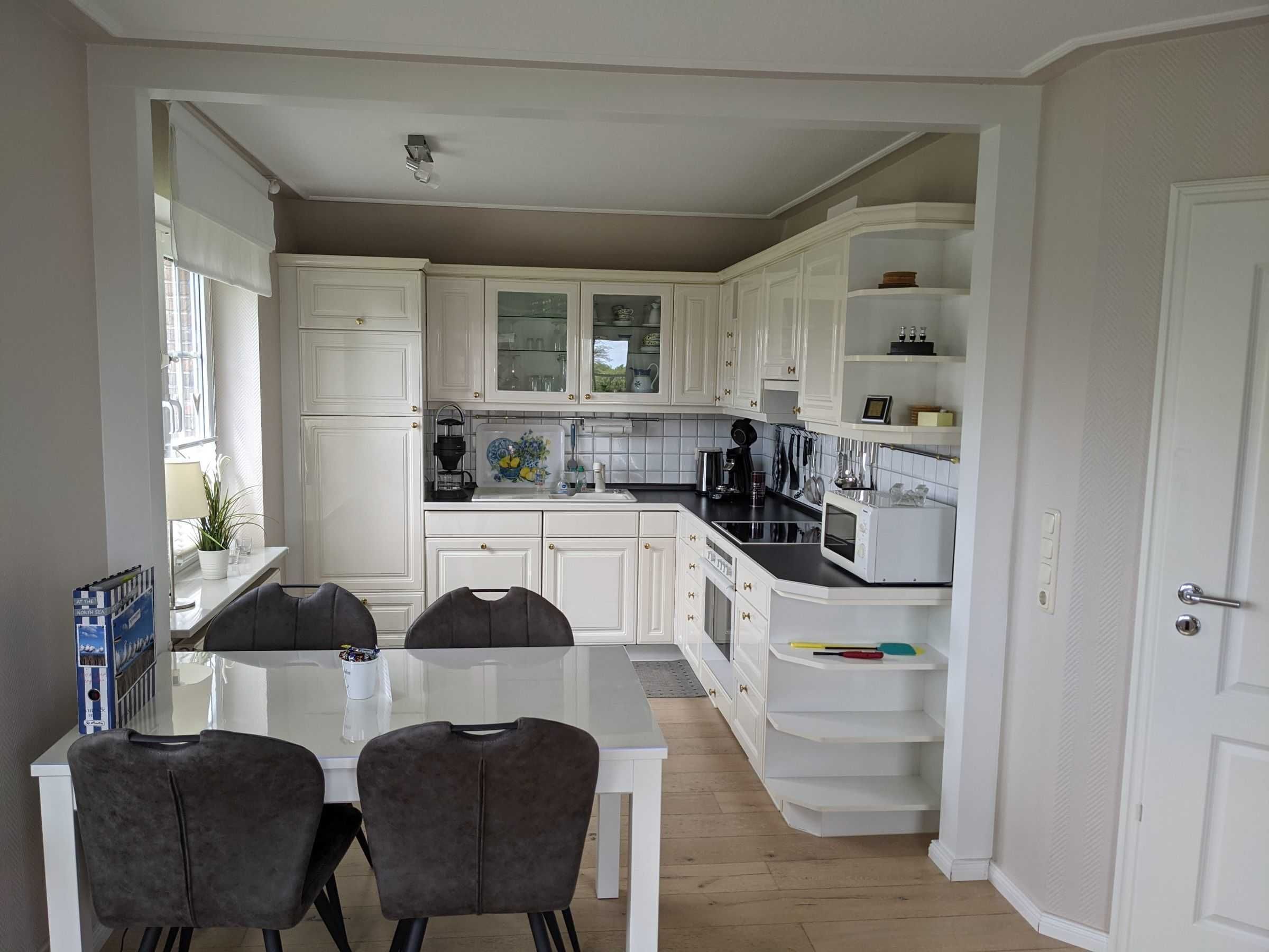 A modern kitchen with white cabinetry, a dining table with chairs, and a built-in microwave.