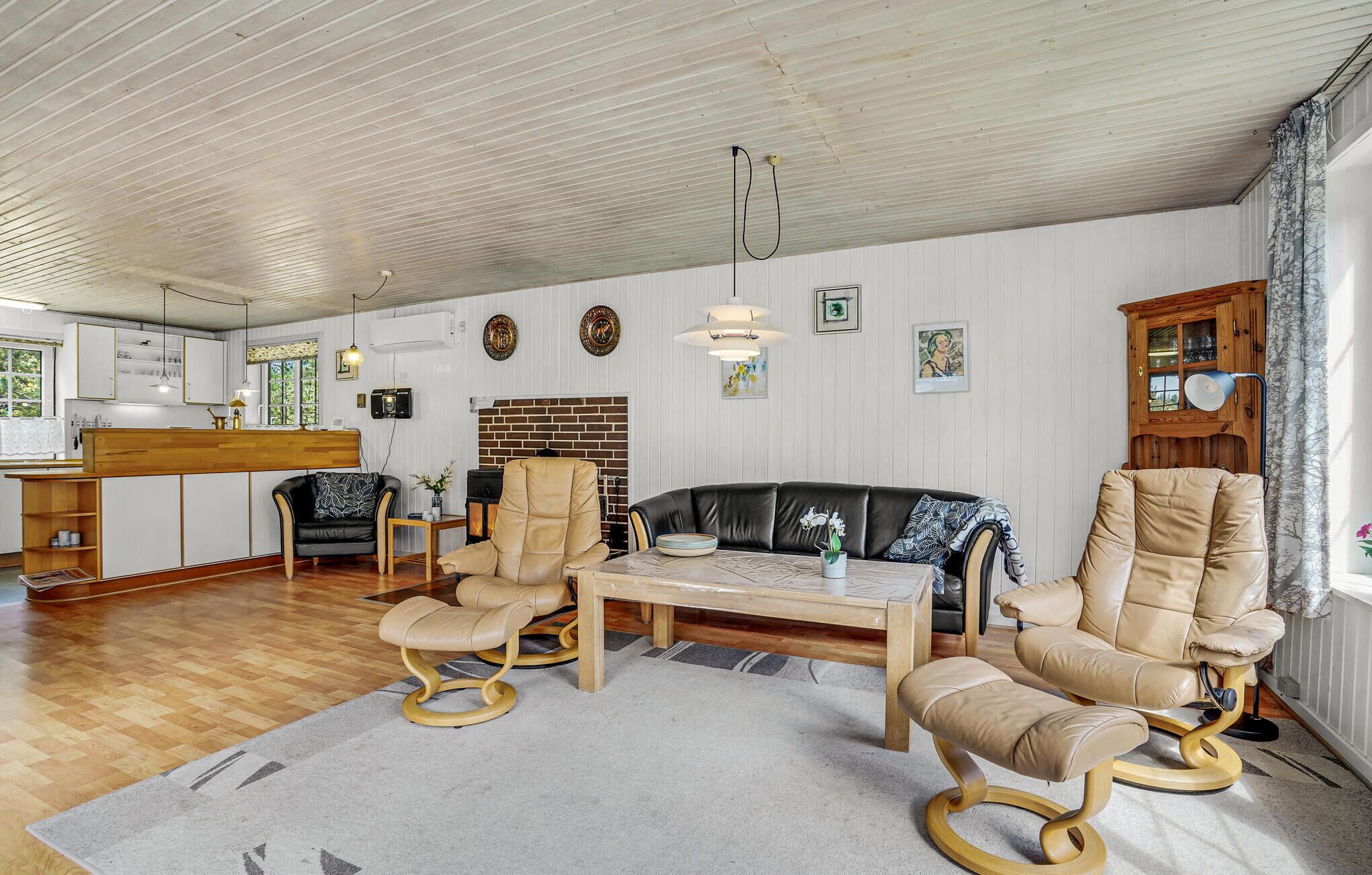 Ett rymligt vardagsrum med ett träpanelat tak, en tegelkamin och en matplats med ett träbord och stolar.