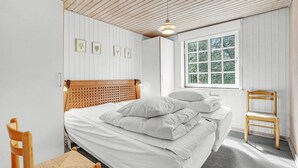 Una camera da letto con testiera in legno, un letto con lenzuola bianche, una finestra vista alberi e una sedia in legno.