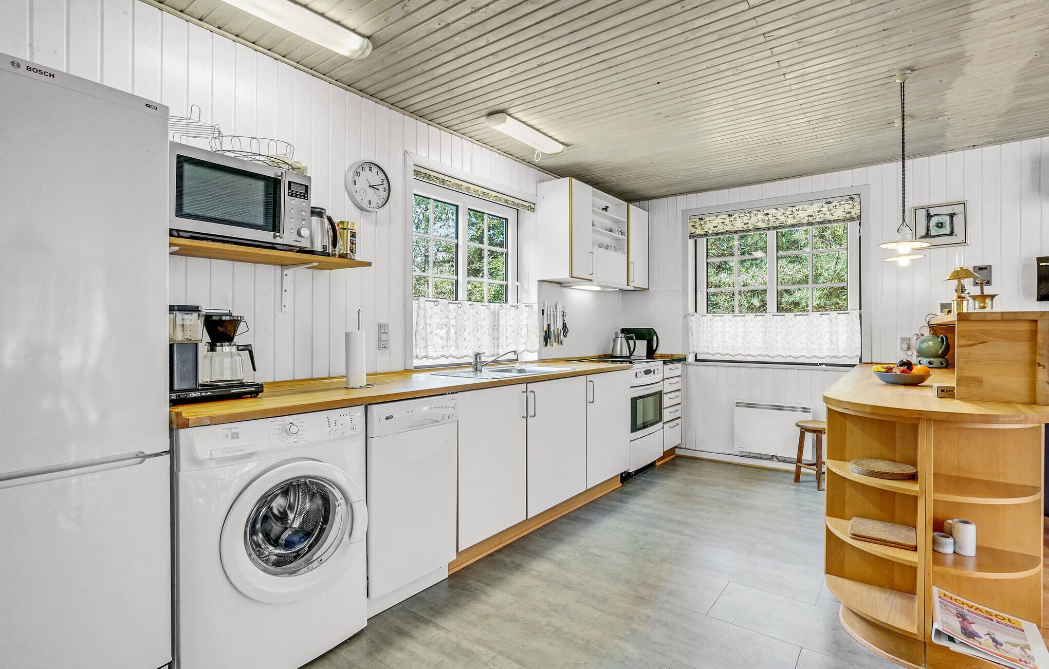 A modern kitchen with white cabinetry, a built-in washing machine, a microwave, and a coffee maker.