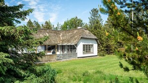 Una casa bianca con tetto di paglia, circondata da rigogliosa vegetazione e alberi.