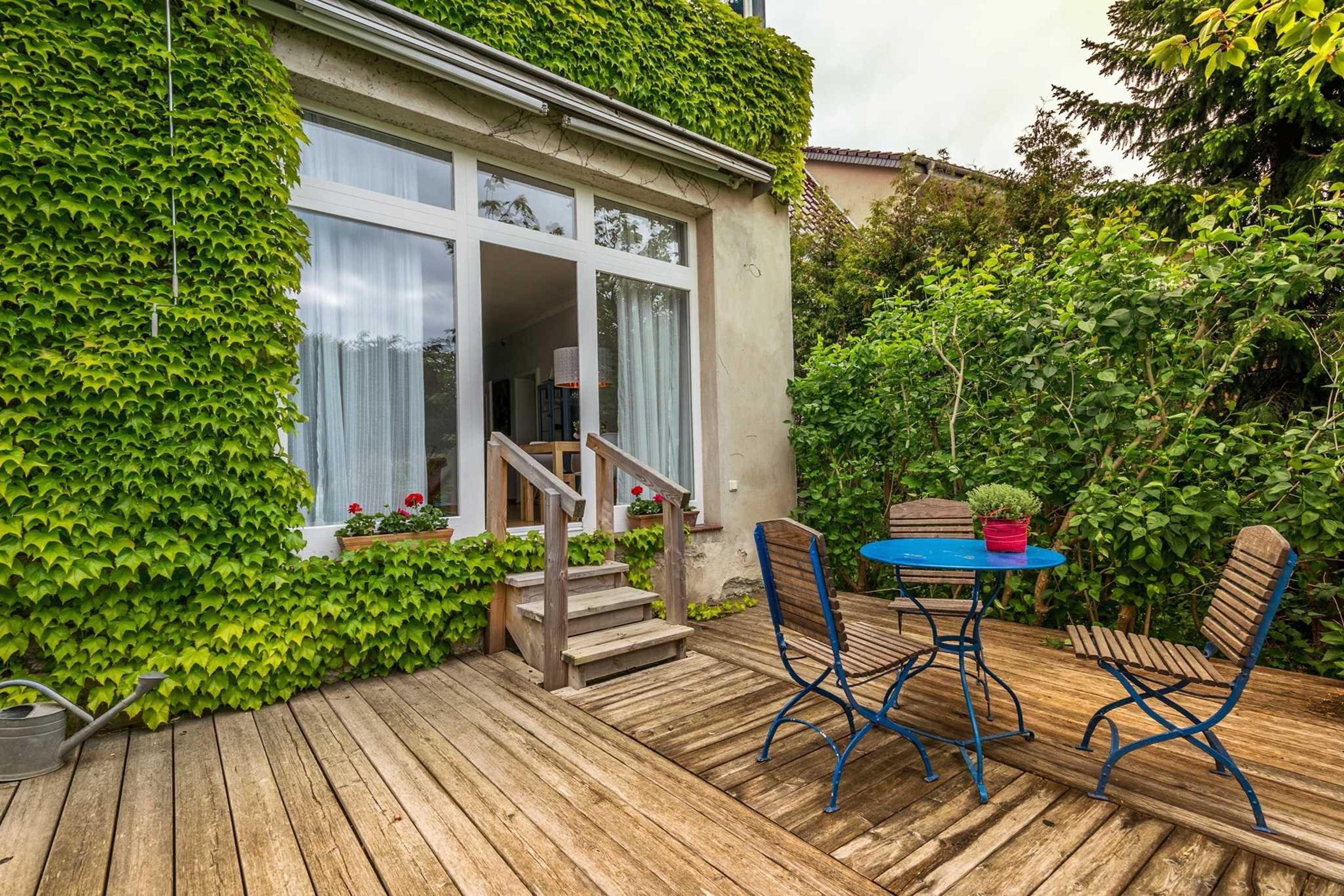 Eine Holzterrasse mit Tisch und Stühlen, einem Blumentopf und einer Treppe, die zu einem Gebäude mit Glastür führt.