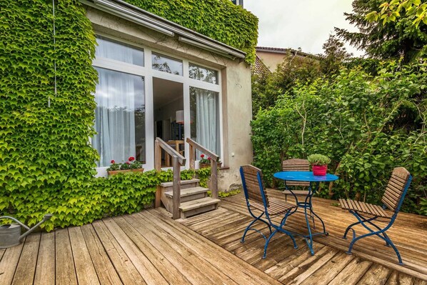 A wooden deck with a table and chairs, a potted plant, and a staircase leading to a building with a glass door. - Muschelsucher - Apartments Proll (Heringsdorf)