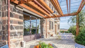 Ein Steinhaus mit einer großen Glasdoor, einer überdachten Terrasse mit Tisch und Stühlen sowie Blick auf die Landschaft.