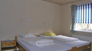Ein Schlafzimmer mit zwei Einzelbetten, einem Holznachttisch, einem Fenster mit blau-weißen Streifen und einem weißen Heizkörper.